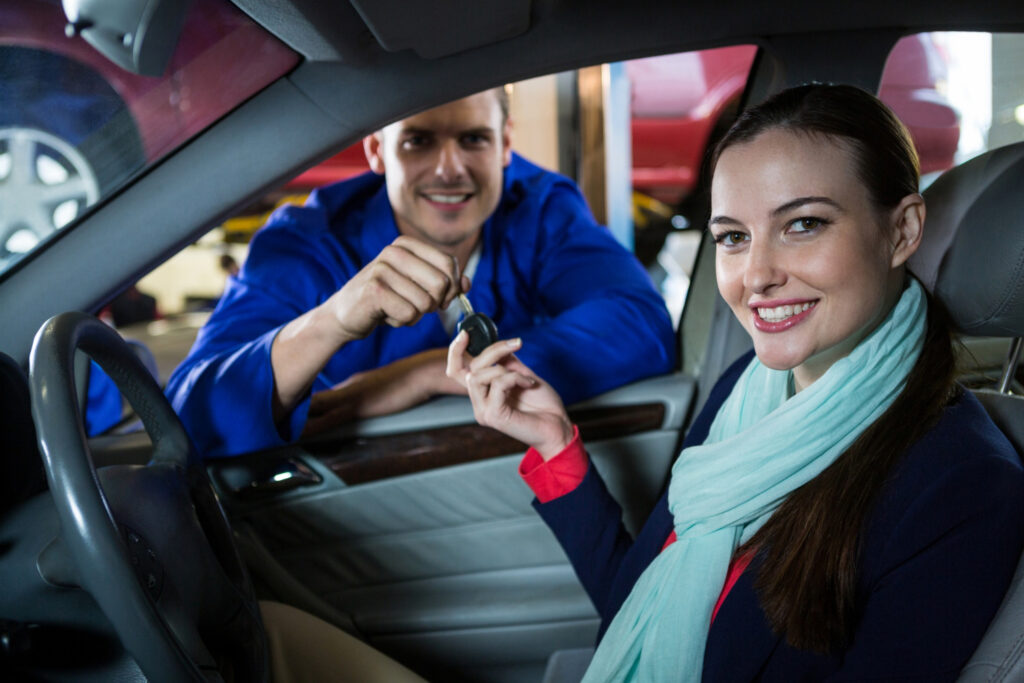 A happy female student sitting in the driver's seat accepting the car keys from her driving instructor after completing her driving classes.