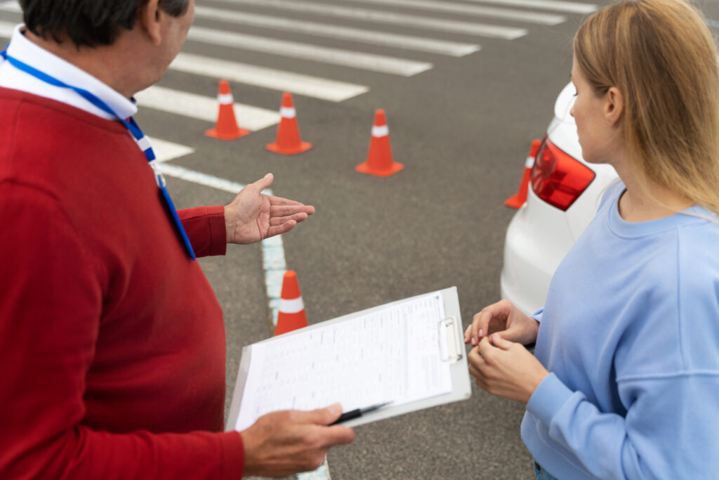 A driving instructor holding a clipboard with a checklist while explaining the G2 road test requirements to a student beside a white car at a DriveTest centre practice course.