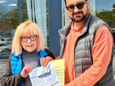 The CEO of an Gclass driving school standing alongside a happy senior adult student holding her official road test results and driver's license.