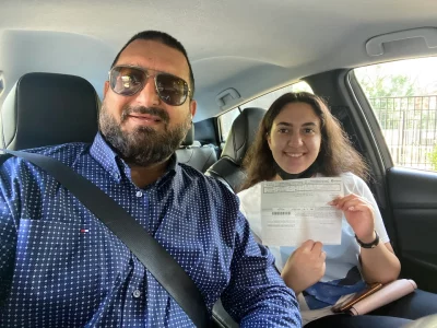 A happy young female student sitting in the passenger seat next to her driving instructor, showing her passed Ontario road test results sheet.